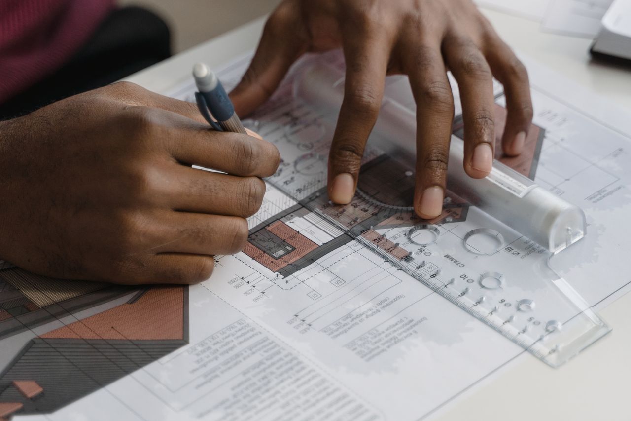 Close-up of architect's hands drawing plans with ruler and pencil, focusing on intricate design details.