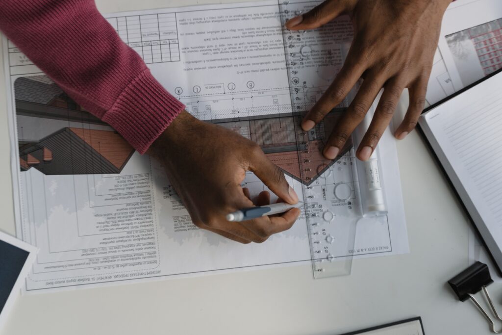 Planning & Building Regulations Architect sketching on blueprints with ruler at desk, designing a building layout.